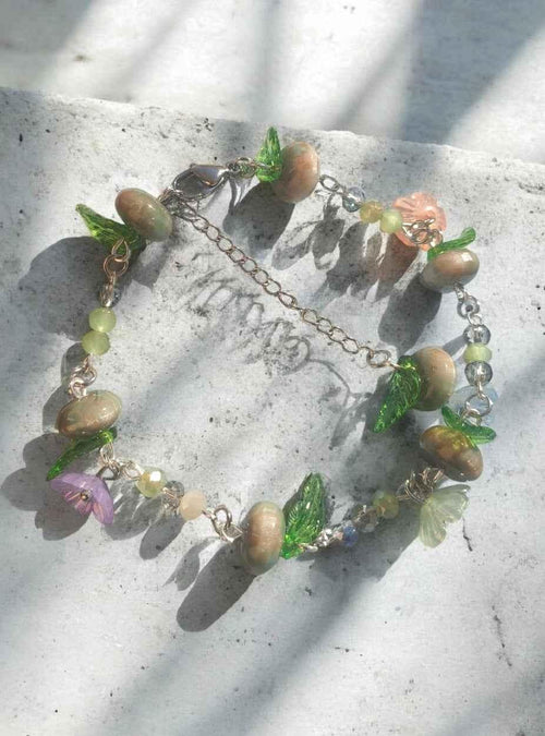 Handgefertigtes Armband mit bunten Glasperlen, Blüten- und Blattcharms auf Betonoberfläche