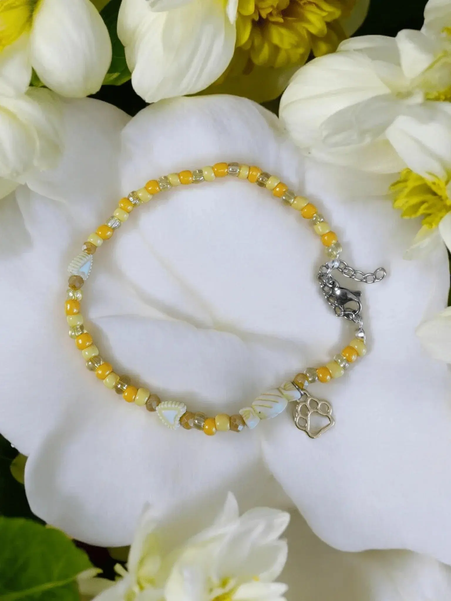 Handgefertigtes Armband mit gelben Perlen, Muscheln und Pfotenanhänger auf weißen Blumen
